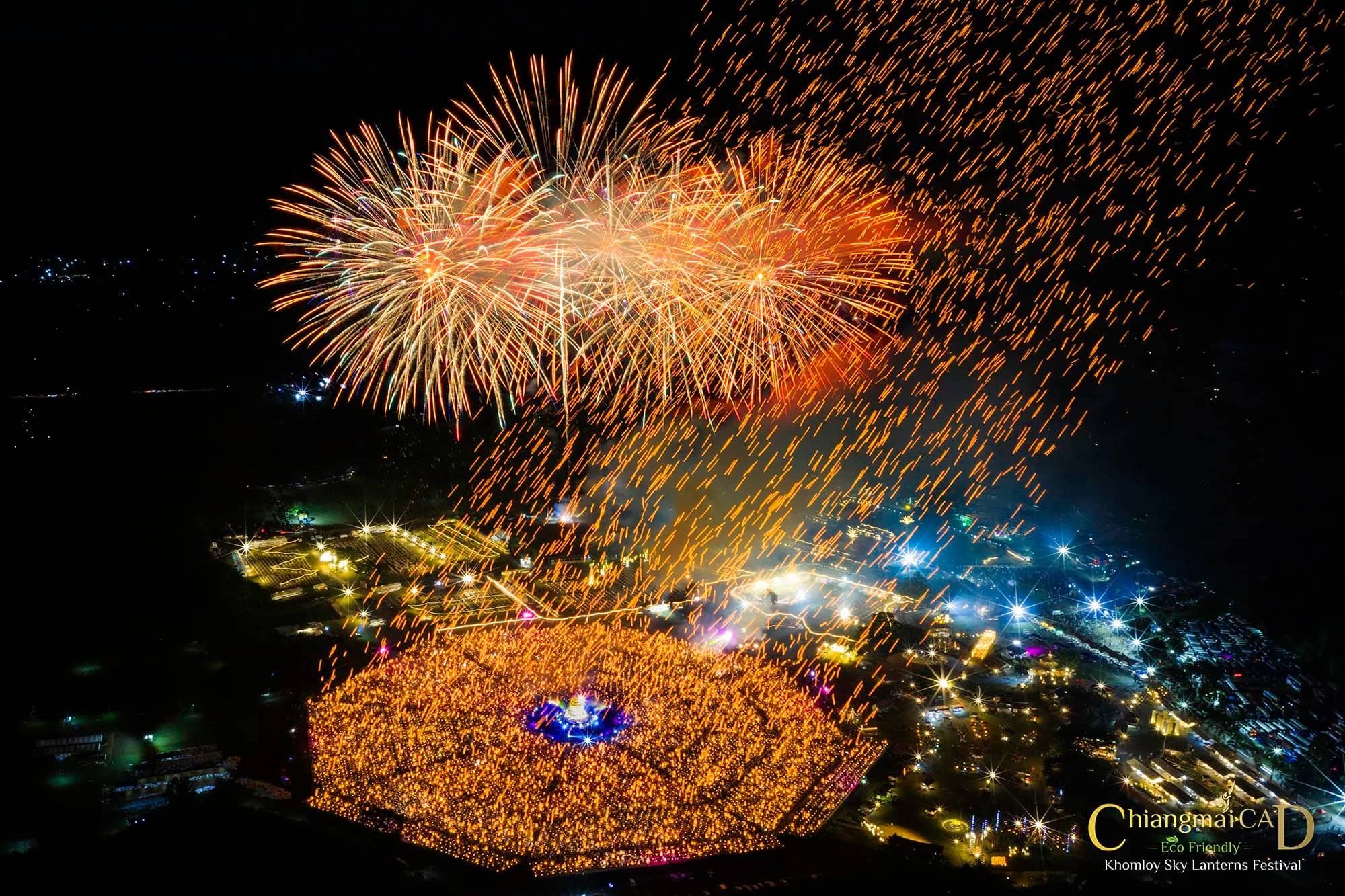 Aerial night view of fireworks bursting above a glowing ring of lanterns at the CAD Khomloy festival in Chiang Mai