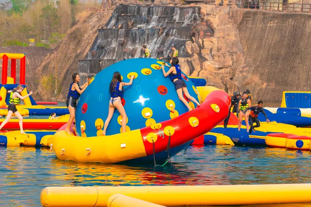 Visitors in life jackets climb a giant inflatable dome on the quarry lake below tall rock walls.