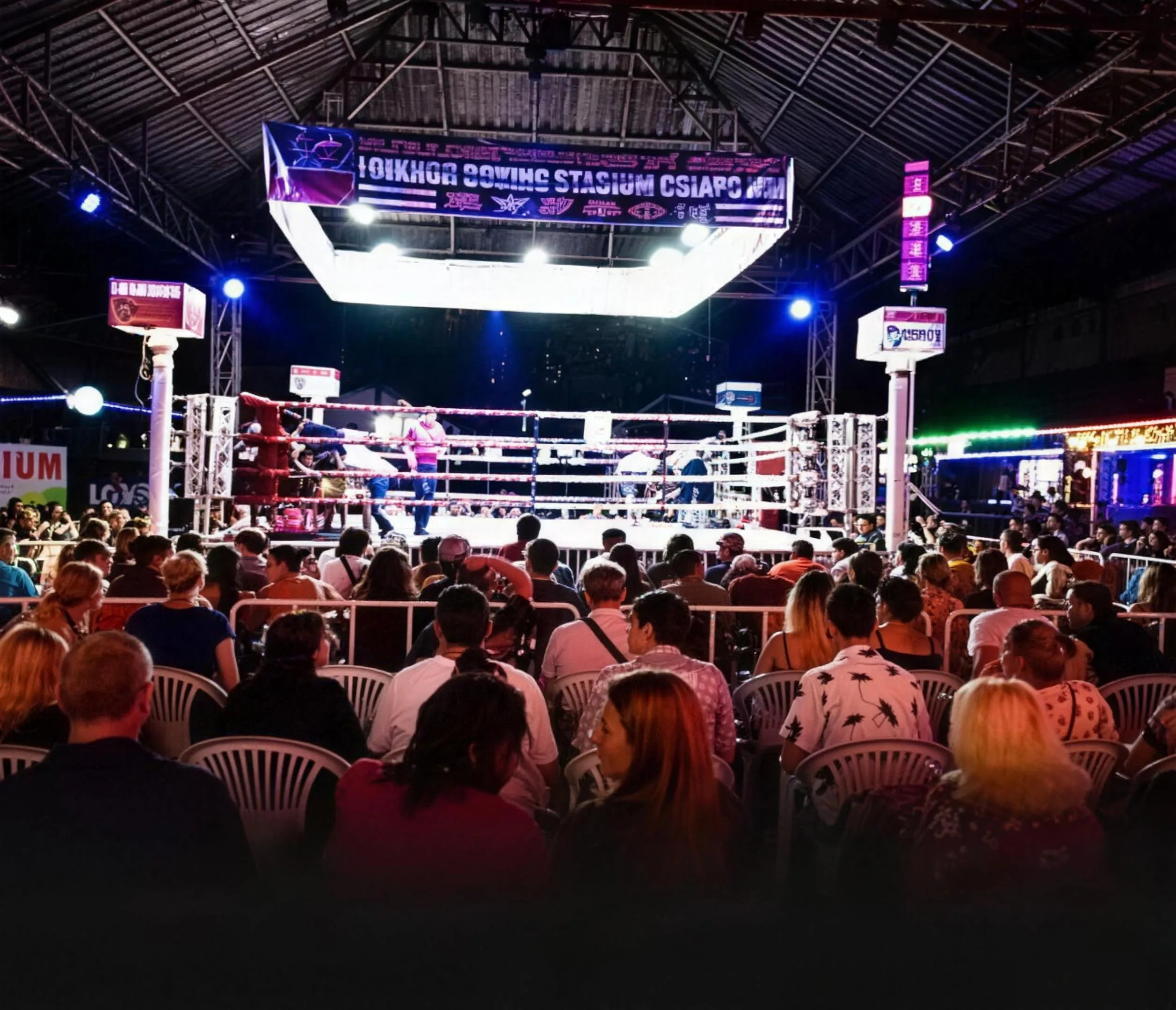 Rows of spectators face the lit boxing ring during a Muay Thai fight night at Loi Kroh Stadium