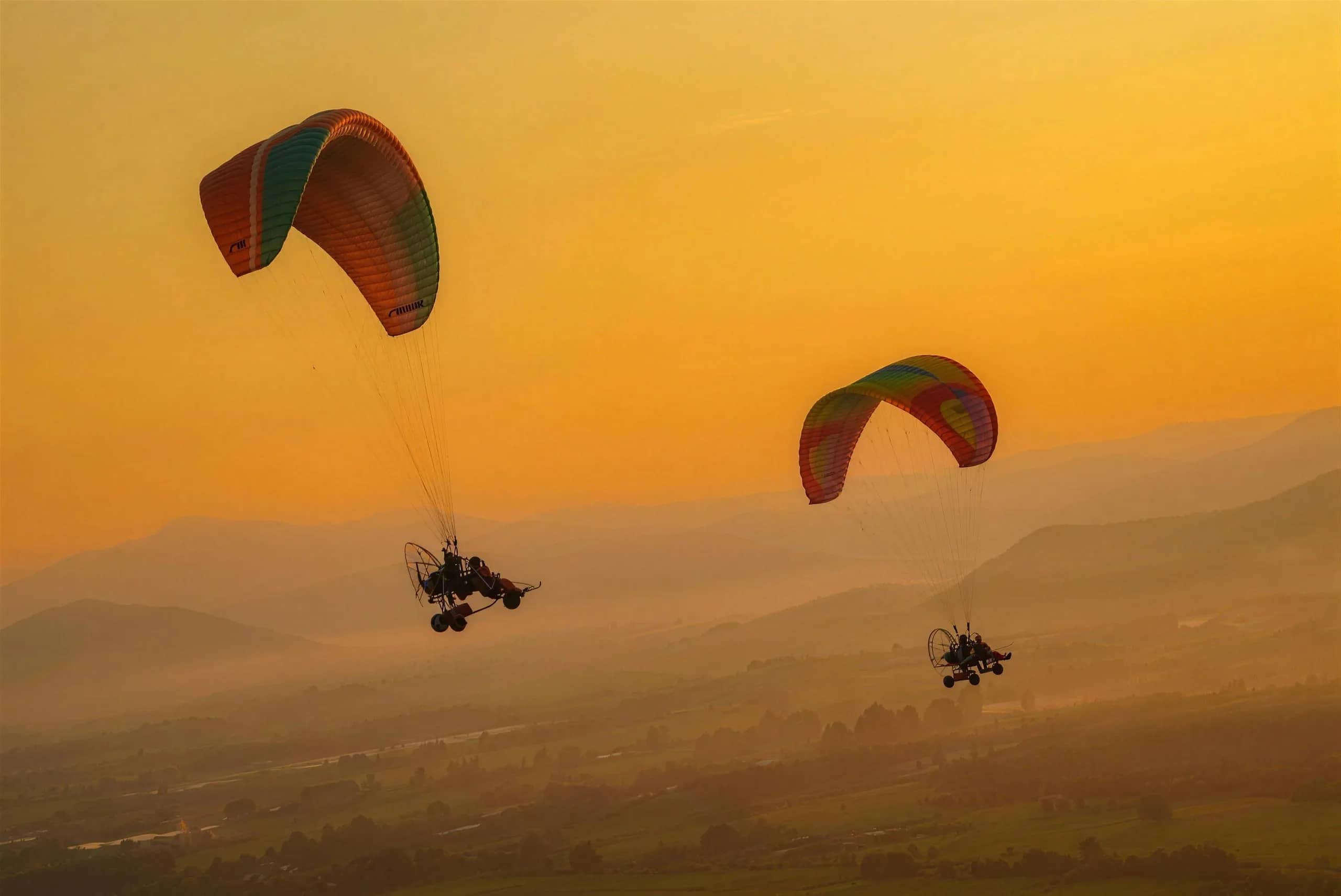 Two paramotor pilots glide above a hazy valley under a warm golden sky near Chiang Mai