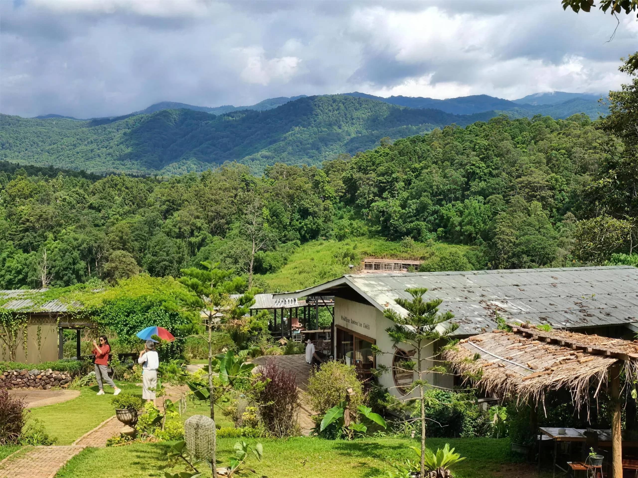 Thatched huts and gardens of Elefin Farm sit below forested mountains near Chiang Mai