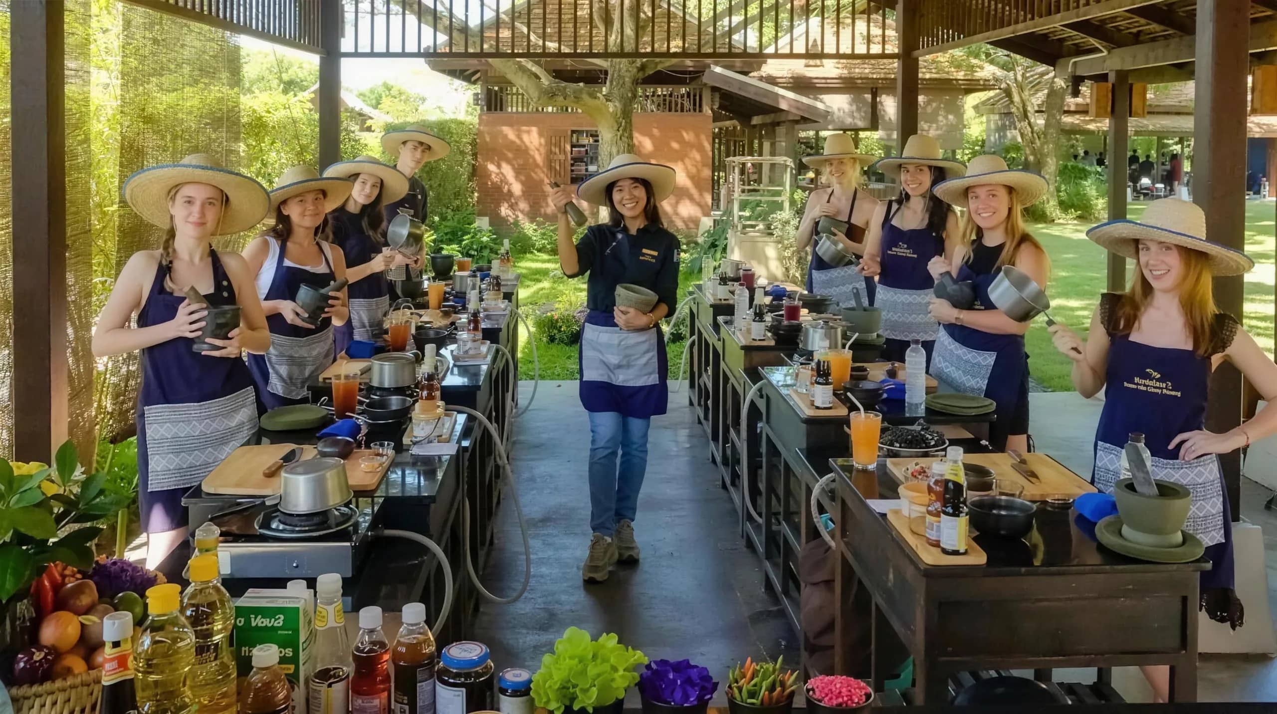 Guests in straw hats and aprons stand at outdoor cooking stations at Grandma's Home Cooking School