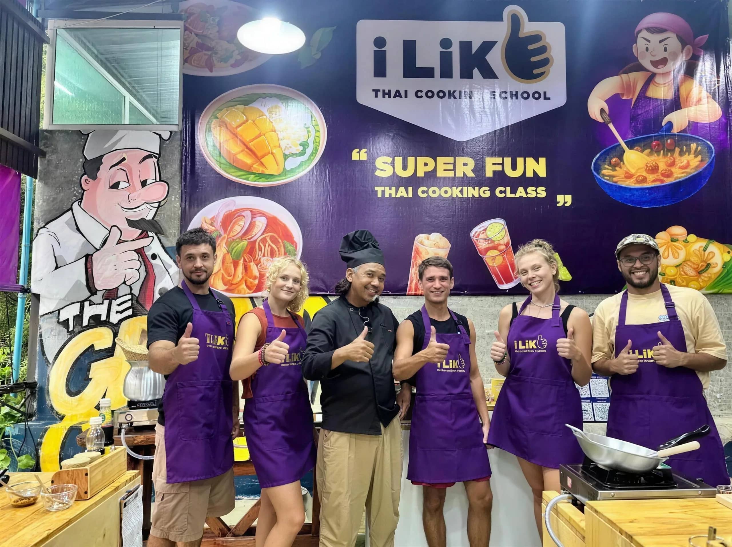 Guests in purple aprons give a thumbs up with their chef at the i-Like Thai Cooking School